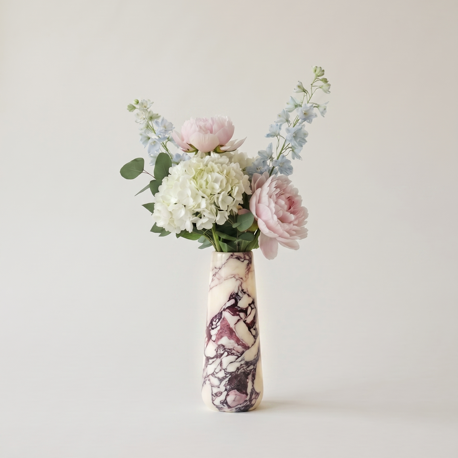Floral arrangement in a calacatta viola marble vase on a plain background